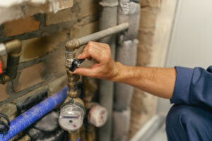 plumber's hand reaches toward water shut off valve to turn it off