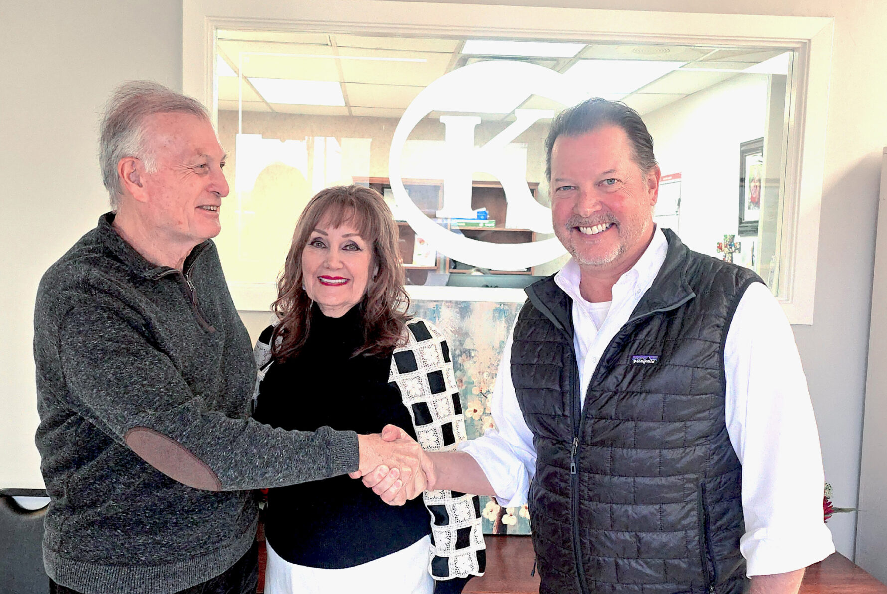 Two men shake hands with a smiling woman between them